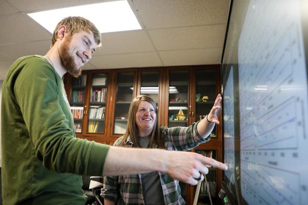 A man and a woman looking at graphs displayed on a smartboard
